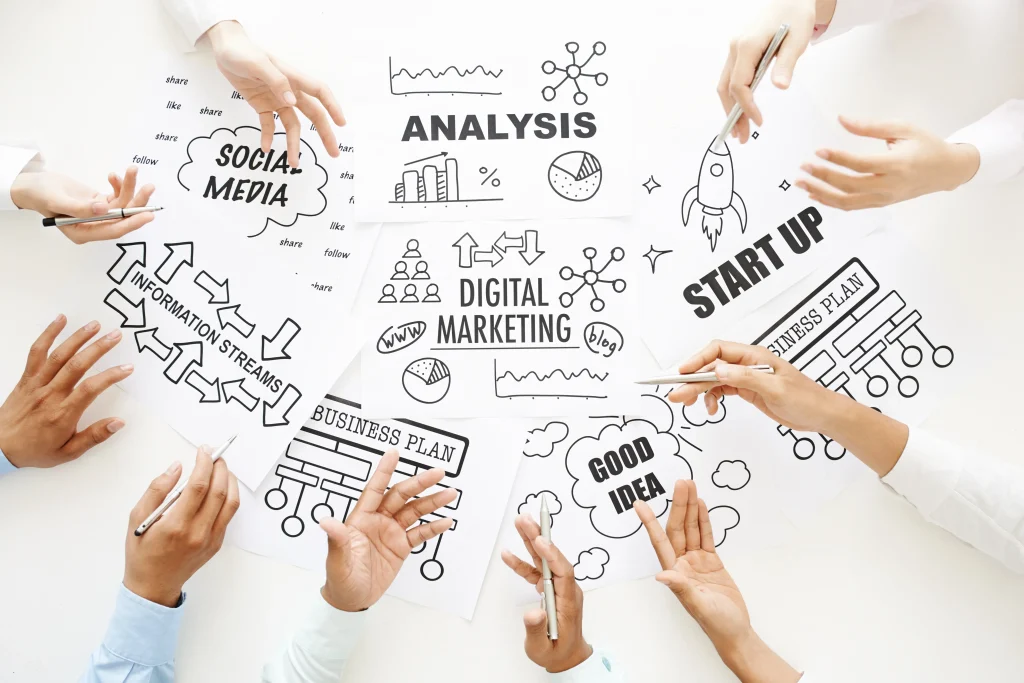 Varias personas colaborando sobre documentos con esquemas de marketing digital, redes sociales y planes de negocio.